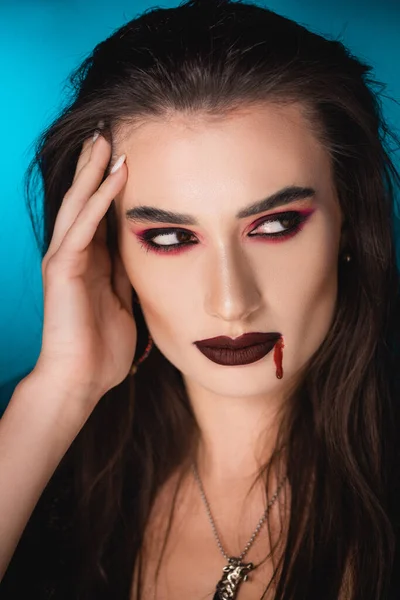 Femme effrayante avec du sang sur le visage regardant loin sur le bleu — Photo de stock