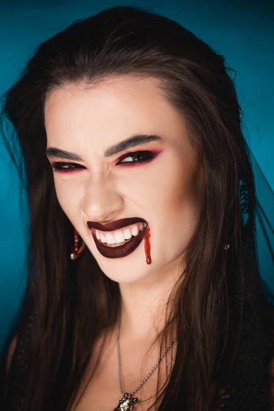 Creepy woman with blood on face showing white teeth on blue — Stock Photo