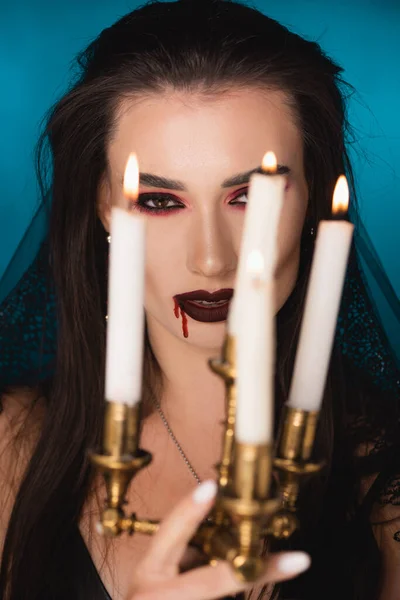 Selective focus of young woman in veil with blood on face near burning candles on blue — Stock Photo