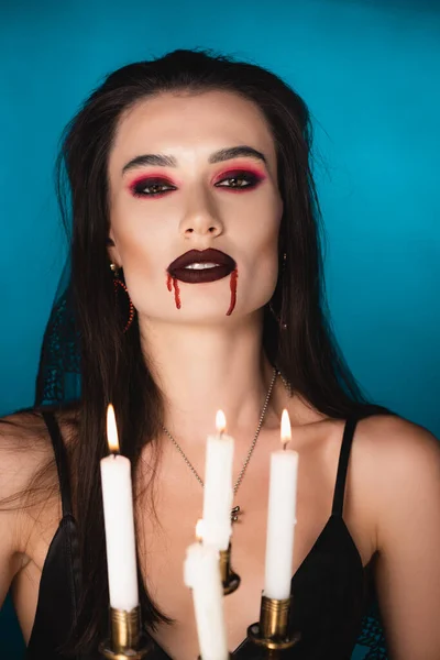 Selective focus of woman with red blood on face near burning candles on blue — Stock Photo
