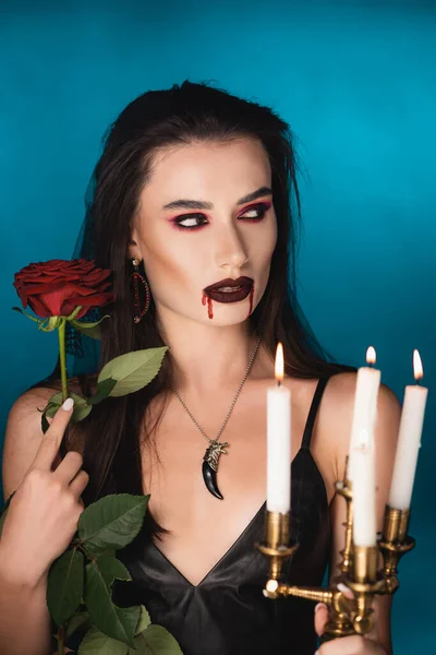 Woman with blood on face holding burning candles and red rose on blue — Stock Photo