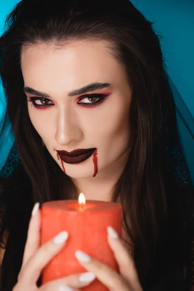 Selective focus of brunette woman with blood on face holding burning candle on blue — Stock Photo