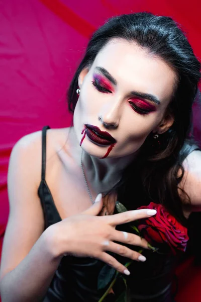 Pale woman with blood on face holding rose on red — Stock Photo