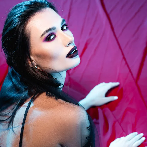 Pale and young woman with makeup looking at camera on red — Stock Photo