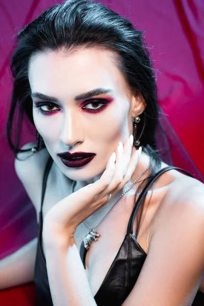 High angle view of pale and young woman looking at camera and touching face on red — Stock Photo