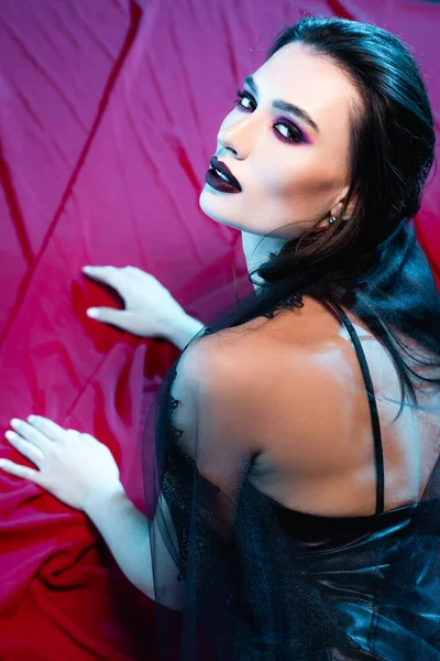 Pale and young woman with black makeup looking at camera on red — Stock Photo