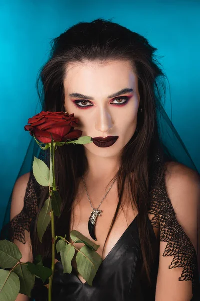 Junge brünette Frau mit dunklem Make-up nahe roter Rose auf blauem Grund — Stockfoto