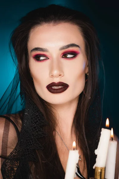 Pale woman with black makeup near burning candles on blue — Stock Photo