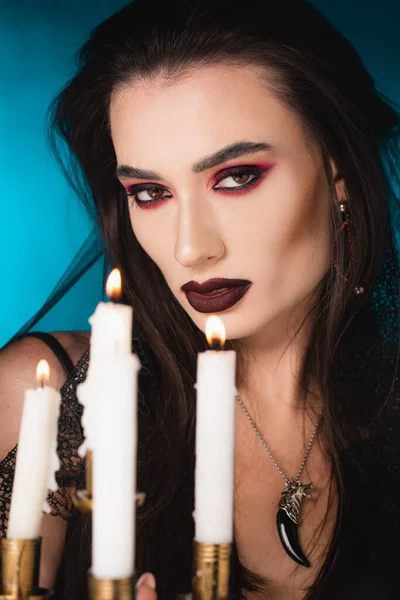 Selective focus of pale woman with black makeup near burning candles on blue — Stock Photo