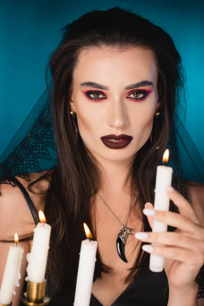 Selective focus of pale young woman with makeup holding burning candle on blue — Stock Photo