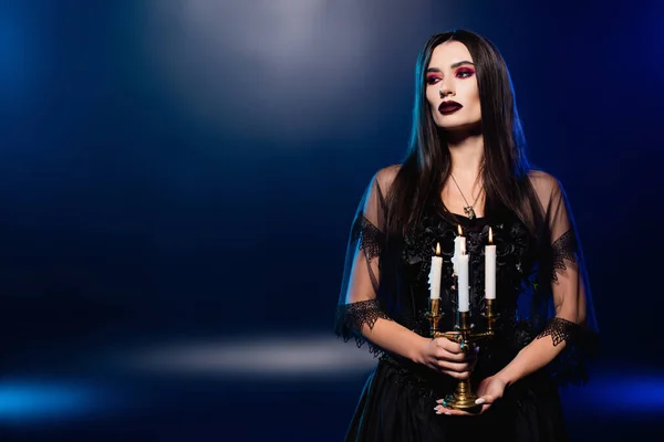 Mulher em vestido preto e véu segurando velas acesas em azul, conceito halloween — Fotografia de Stock