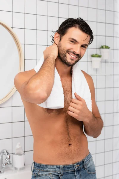 Hombre sin camisa sonriendo a la cámara mientras sostiene la toalla en el baño - foto de stock