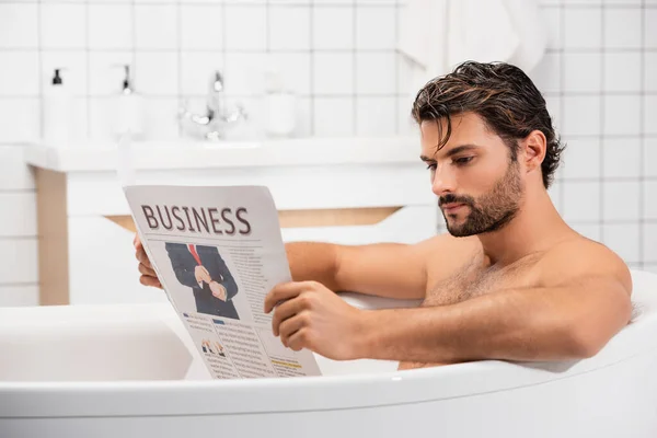 Bearded man reading business newspaper while taking bath — Stock Photo