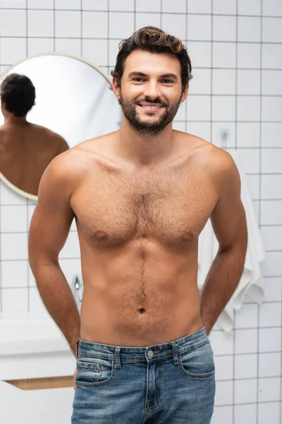 Homem musculoso em jeans sorrindo para a câmera no banheiro — Fotografia de Stock