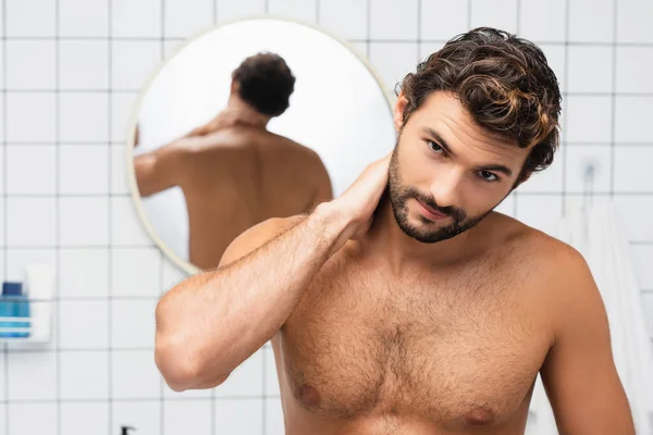 Мужчина без рубашки касается шеи, глядя в камеру в ванной комнате — стоковое фото