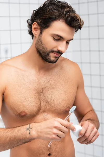 Homem sem camisa segurando escova de dentes e pasta de dentes no banheiro — Fotografia de Stock