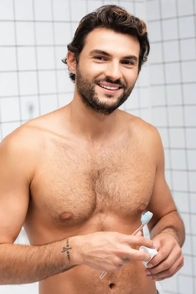 Homme musclé souriant à la caméra tout en tenant la brosse à dents et le tube de dentifrice — Photo de stock