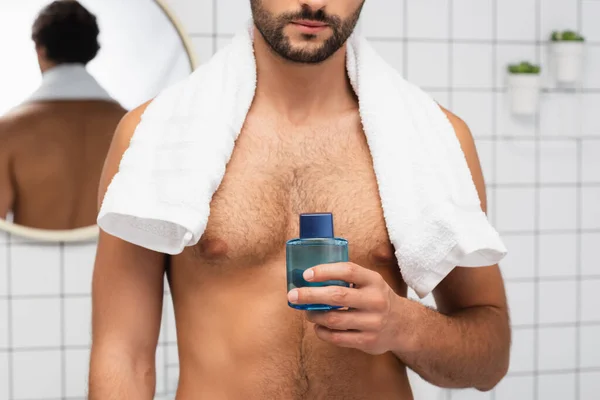 Cropped view of shirtless man with towel around neck holding after shaving lotion in bathroom — Stock Photo