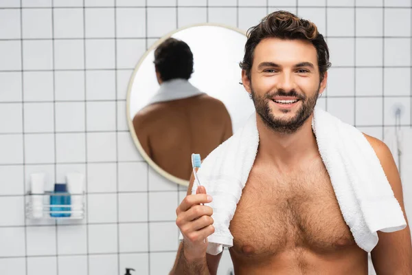 Усміхнений без сорочки чоловік з рушником навколо шиї тримає зубну щітку у ванній — стокове фото