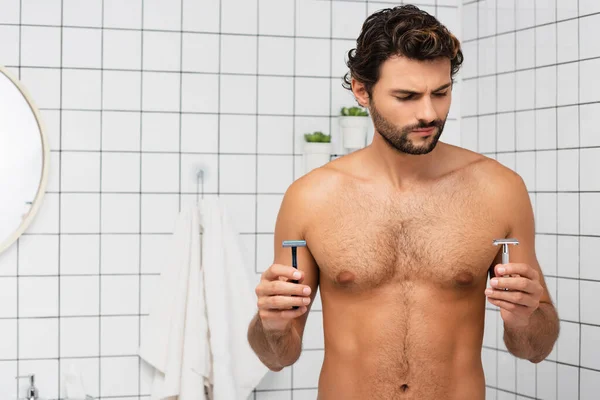 Homem muscular segurando navalhas no banheiro em casa — Fotografia de Stock