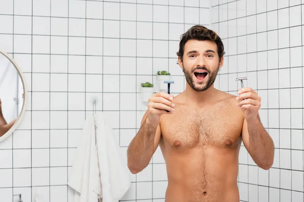 Homme torse nu excité tenant des rasoirs dans la salle de bain — Photo de stock