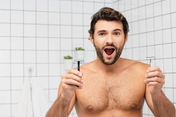 Захоплений без сорочки чоловік дивиться на камеру, тримаючи бритви у ванній — стокове фото