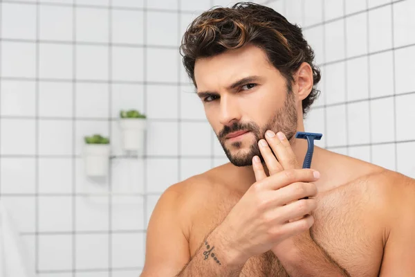 Shirtless man touching cheek while shaving in bathroom — Stock Photo