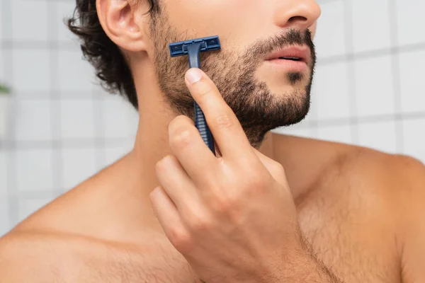 Vista recortada del hombre barbudo afeitándose con afeitadora desechable en el baño - foto de stock