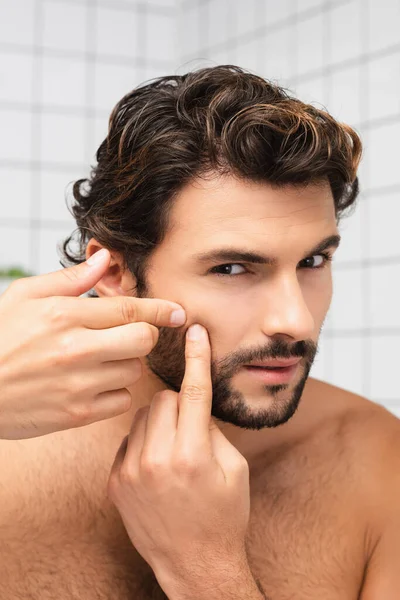 Uomo senza maglietta toccare la pelle sulla guancia e guardando la fotocamera in bagno — Foto stock