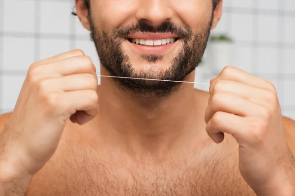 Cropped view of bearded man smiling while holding dental floss in bathroom — Stock Photo