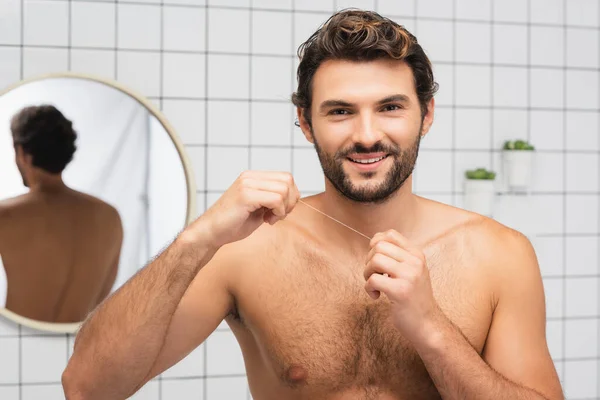 Uomo a torso nudo che sorride alla macchina fotografica mentre tiene il filo interdentale in bagno — Foto stock