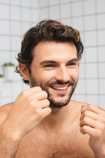 Uomo sorridente che tiene filo interdentale e distoglie lo sguardo in bagno — Foto stock