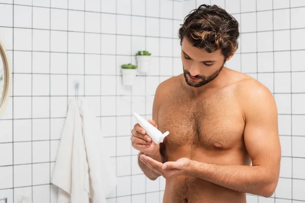 Muscular man squeezing cosmetic cream from tube in bathroom — Stock Photo