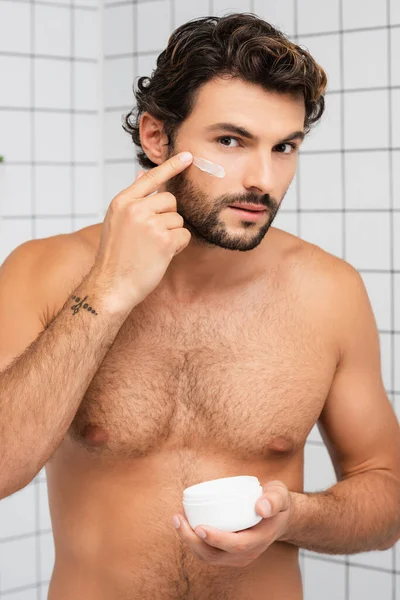 Hombre sin camisa aplicando crema cosmética en la cara en el baño - foto de stock