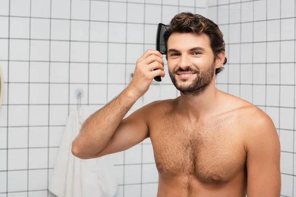 Sorrindo muscular homem pentear o cabelo no banheiro — Fotografia de Stock