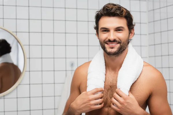 Sorridente uomo senza maglietta toccare asciugamano e guardando la fotocamera in bagno — Foto stock