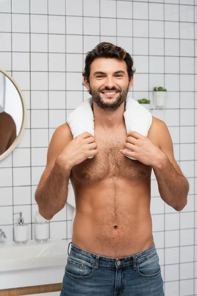 Hombre musculoso sonriendo a la cámara mientras sostiene la toalla en el baño - foto de stock
