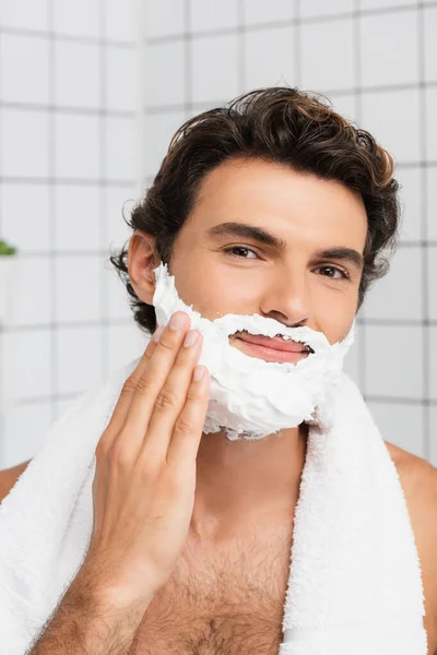 Uomo sorridente guardando la fotocamera mentre si applica schiuma da barba — Foto stock