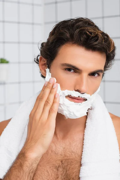 Brunette homme avec serviette autour du cou appliquer de la mousse à raser — Photo de stock