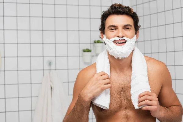 Allegro uomo senza maglietta con schiuma da barba sul viso che tiene asciugamano in bagno — Foto stock