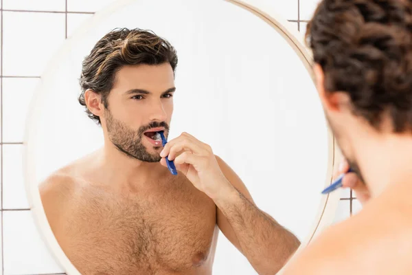 Uomo senza maglietta lavarsi i denti mentre si guarda specchio in bagno — Foto stock