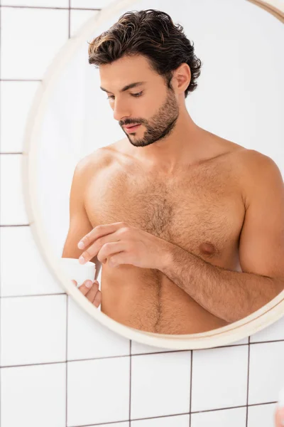 Uomo senza maglietta che tiene il vaso con crema cosmetica in bagno — Foto stock