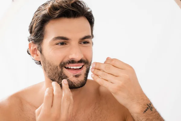 Hombre sin camisa sonriendo y sosteniendo hilo dental en el baño - foto de stock