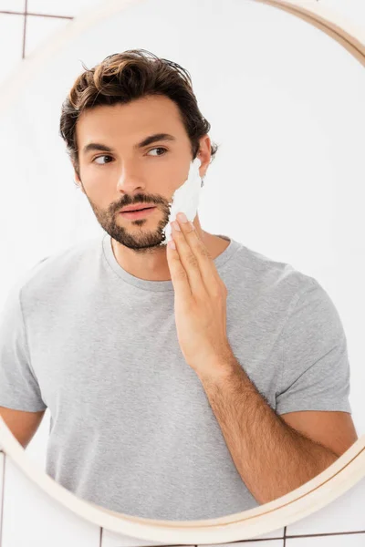 Bärtiger Mann schaut in Spiegel, während er im Badezimmer Rasierschaum aufträgt — Stockfoto