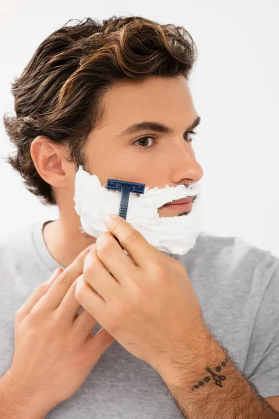 Young man with foam on face shaving with razor isolated on grey — Stock Photo