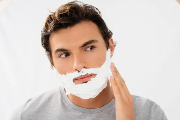 Hombre morena aplicando espuma de afeitar sobre fondo gris sobre fondo gris - foto de stock