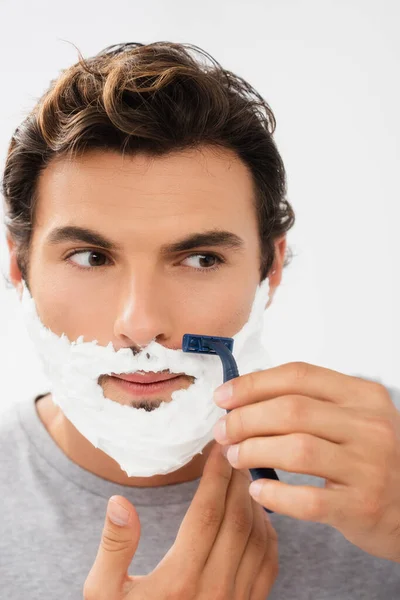 Giovane uomo con schiuma sulla rasatura del viso con rasoio monouso isolato su grigio — Foto stock