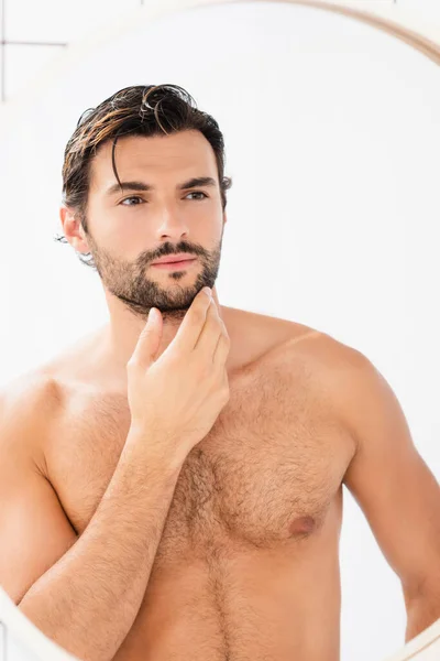 Homme sans chemise avec les cheveux mouillés toucher menton tout en regardant miroir — Photo de stock