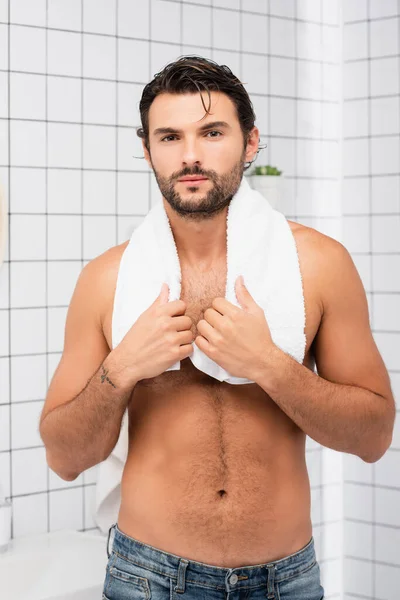 Дерьмовый мужчина с мокрыми волосами и полотенцем смотрит в камеру в ванной комнате — стоковое фото