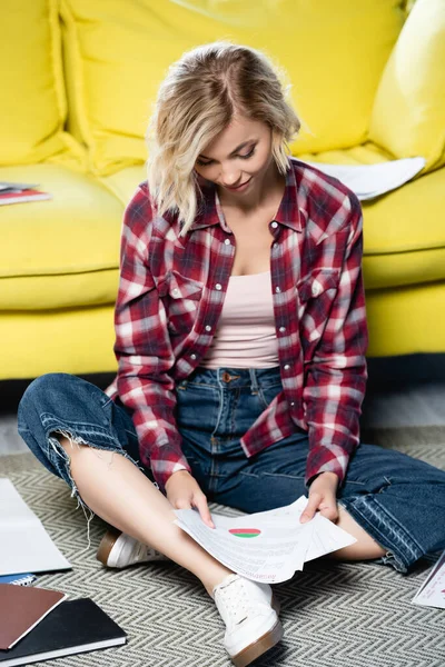 Jeune femme blonde assise sur le sol et regardant à travers les documents — Photo de stock